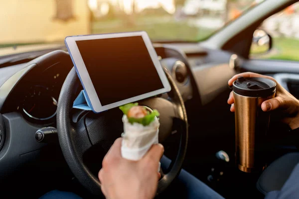 L'autista guarda film o programmi TV sul tablet durante il pranzo. Mi fermo a mangiare un boccone. L'uomo mangia snack in macchina e beve caffè o tè . — Foto Stock