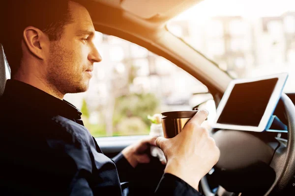O motorista assiste a filmes ou programas de TV no tablet durante o almoço. A parar para comer qualquer coisa. Homem come lanche no carro e bebe café ou chá . — Fotografia de Stock