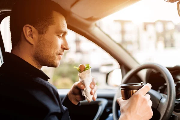 Mi fermo a mangiare un boccone. L'uomo mangia snack in macchina e beve caffè o tè . — Foto Stock