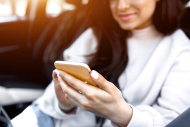 Genç bir kadın arabada oturuyor. Güzel esmer model akıllı telefon ya da telefon kullanıyor.