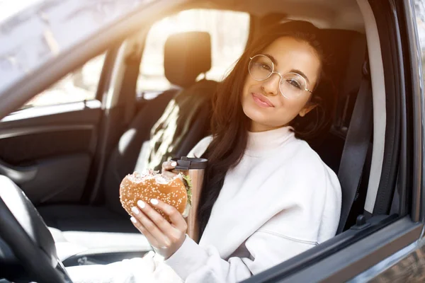 Еда на дорогах. Женщина ест гамбургер и пьет кофе или чай из термоса. Концепция "Еда на дороге" . — стоковое фото