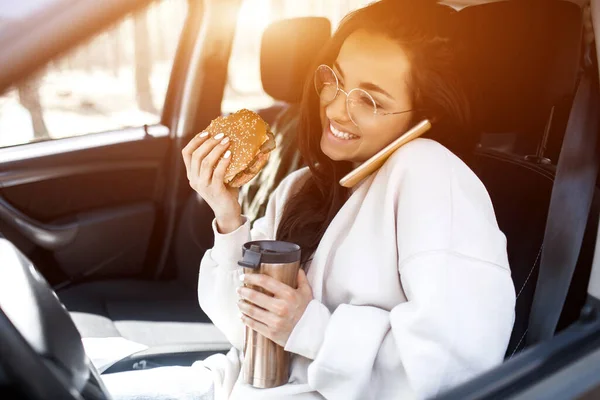 Еда на дорогах. Женщина ест гамбургер и пьет кофе или чай из термоса. Концепция "Еда на дороге" . — стоковое фото