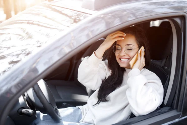 Egy fiatal nő ül az autóban. Gyönyörű barna modell használ okostelefon vagy telefon — Stock Fotó
