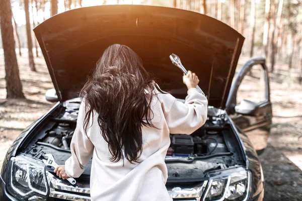 O carro avariou. Acidente na estrada. Uma mulher abriu o capô e verifica o motor e outros detalhes do carro — Fotografia de Stock