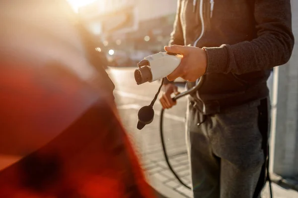 Homem segurando cabo de carregamento de energia para carro elétrico no parque de estacionamento ao ar livre. E ele vai ligar o carro à estação de carregamento no estacionamento perto do centro comercial. — Fotografia de Stock