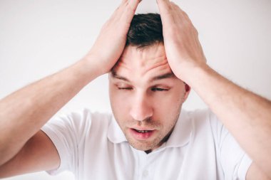 Genç hasta bir adam beyaz arka planda izole edilmiş. Adam baş ağrısı yüzünden el ele tutuşuyor. Acıdan muzdarip. Hasta, hasta, gözleri kapalı genç bir adam..