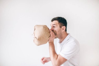 Genç hasta bir adam beyaz arka planda izole edilmiş. Adam torbaya kusuyor. Astım ya da sindirim bozukluğundan muzdarip. Stüdyoda yalnız bir adamın yan görüntüsü.