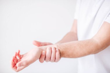 Genç adam beyaz arka planda izole edilmiş. Yaklaş ve kesme görüntüsü ver. Ağrı ve ağrıdan dolayı elini bileğinden tut..