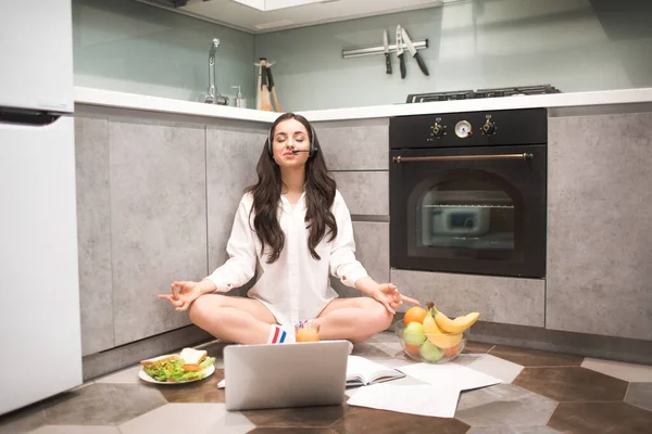 Vacker svarthårig kvinna arbetar hemifrån. En kvinnlig modell sitter på köksgolvet i en yogapose. Slutet på ett balanserat och lugnt arbete. Känns full Zen, lugn och ro. — Stockfoto