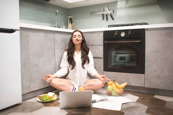 Güzel siyah saçlı kadın evde çalışıyor. Kadın bir model mutfak zemininde yoga pozunda oturuyor. Dengeli ve sakin bir işin sonu. Zen, huzur ve sükunet dolu hissettiriyor..