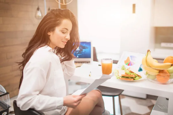 Piękna czarnowłosa kobieta pracuje w domu. Pracownik siedzi w kuchni i ma dużo pracy na laptopie i tablecie i ma wideokonferencje i spotkania. — Zdjęcie stockowe