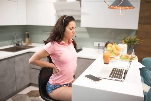 Local de trabalho desconfortável. Mulher bonita trabalha a cozinha em casa ela está muito cansada. Mas ainda há muito trabalho. Trabalhar em casa é difícil e cansativo. Modelos femininos têm dor no pescoço e nas costas — Fotografia de Stock