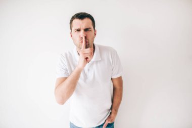 Genç adam beyaz arka planda izole edilmiş. Stüdyoda tek başına duran ve dudağını tutan adam. Hush sembolü. Sessizlik ve sessizlik.