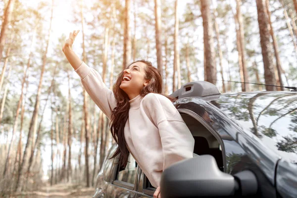 Jovem feliz saiu da janela de um carro. Viajando de carro na floresta. Viagem de campo. Férias de carro — Fotografia de Stock