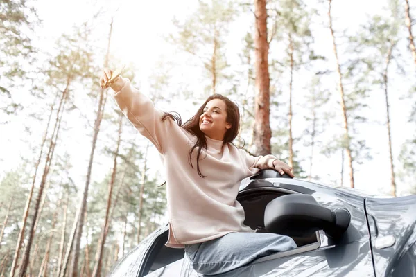 Jovem feliz saiu da janela de um carro. Viajando de carro na floresta. Viagem de campo. Férias de carro — Fotografia de Stock