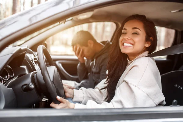 Instrução de condução. Uma jovem aprende a conduzir um carro. Seu instrutor ou namorado não gosta da maneira como ela dirige um carro. Mas a menina está satisfeita consigo mesma e não ouve o cara . — Fotografia de Stock