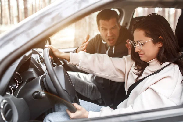 Driving instruction. A young woman learns to drive a car for the first time. She does not work well. Her husband or instructor yells at her. She is crying — Stock Photo, Image