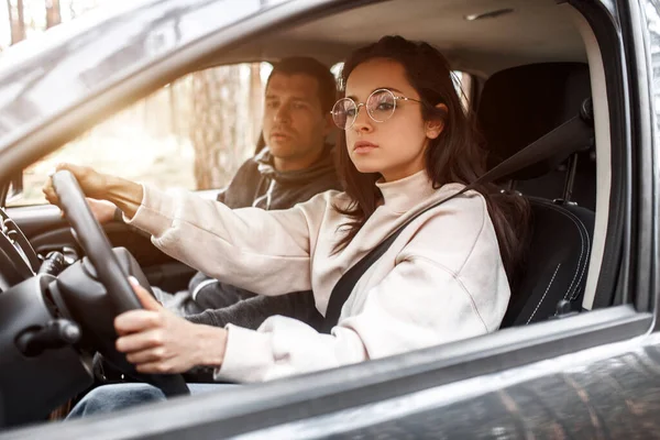 Driving instruction. A young woman learns to drive a car for the first time. Her instructor or boyfriend helps her and teaches her — Stock Photo, Image