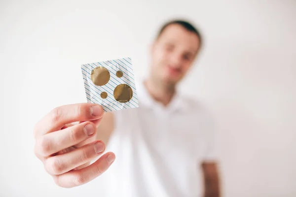 Young man isolated over white background. Blurred defocused guy holding packed condom in hand and show it on camera. Safe intimacy and sex. — Stock Photo, Image