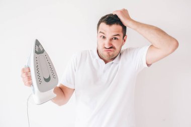 Genç adam beyaz arka planda izole edilmiş. Adam demiri elinde tutuyor ve ne yapacağını bilemiyor. Fotoğraftaki kafası karışmış korkmuş adam..