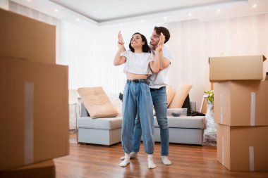 Oturma odasındaki boş kutuların yanında genç evli bir çift. Yeni evlerinden memnunlar. Taşınmak, ev almak, apartman konsepti..