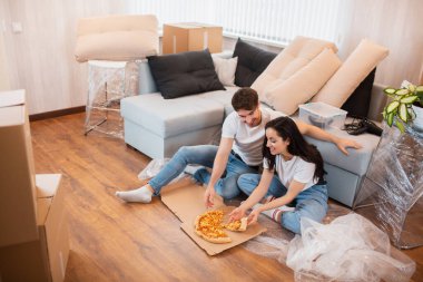 Taşınırken pizza yiyen mutlu bir aile. Genç bir çiftin yeni evde birlikte otururken dinlenirken çekilmiş fotoğrafı..