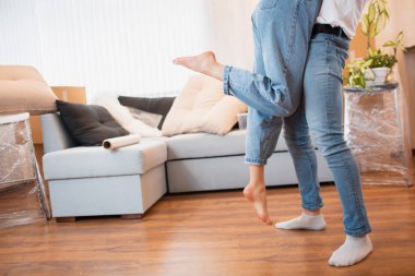 Bacaklar görüş açısını kapatsın. Genç çiftin ilk kez ev sahipleri taşınma günü konseptini kutluyorlar, koca karısını kaldırıyor yeni evinde kutuların yanında duruyor, taşınma yeri ve aile ipoteği..