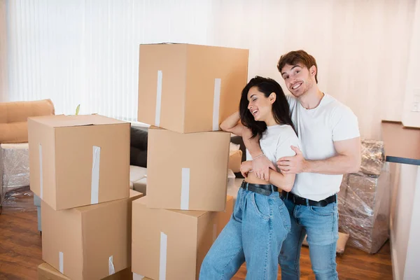 Ein junges Ehepaar steht im Wohnzimmer des Hauses neben ausgepackten Kartons. Sie freuen sich über ein neues Zuhause. Umzug, Hauskauf, Wohnungskonzept. — Stockfoto