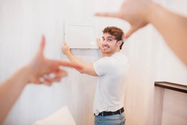 O casal mudou-se para casa nova. foto close-up de mãos femininas enquanto decora novo apartamento, homem pendurado imagem ou moldura de foto na parede — Fotografia de Stock