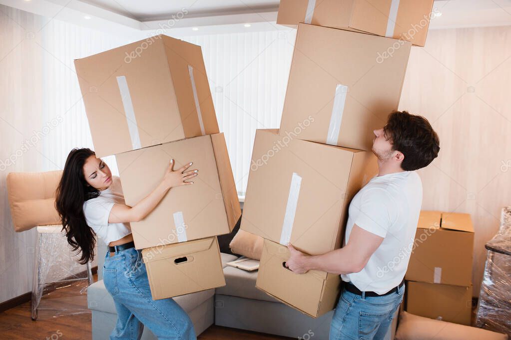Young couple carrying many cardboard boxes one by one at new home. Moving house.