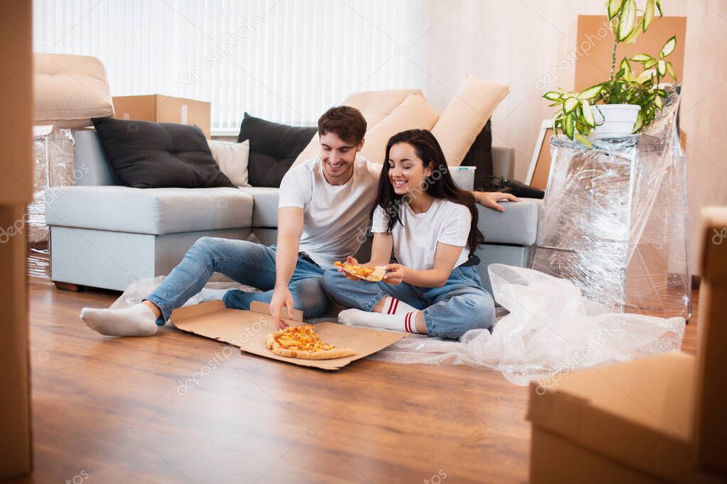 Happy family eating pizza on moving day. Picture of a young couple enjoying rest time while sitting together in the new house.