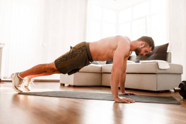Genç adam spor için evine git. Tam boy tişörtsüz sporcunun resmi odada tek başına kalas pozisyonunda duruyor. Acemi, elinden gelenin en iyisini yapmaya ve egzersiz yapmaya çalışır. Çalışkan gerçek bir insan.