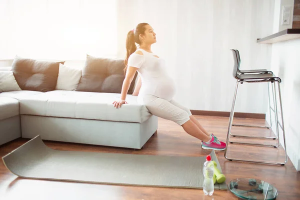 Hamile kadın evde kanepe kullanarak egzersiz yapıyor. — Stok fotoğraf