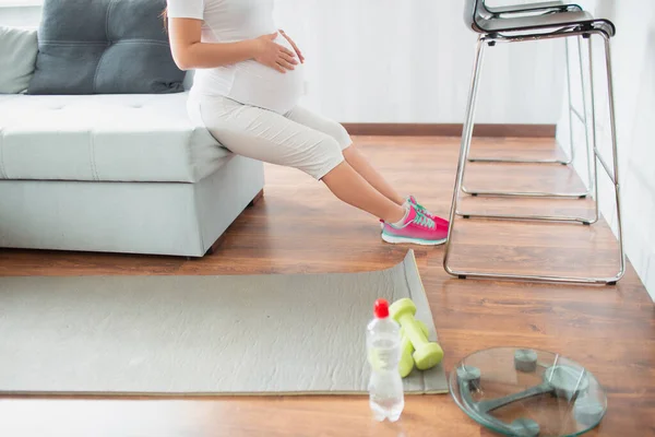 Pregnant black-haired woman doing workout at home using a sofa — Stock Photo, Image