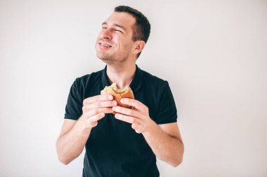 Genç adam beyaz arka planda izole edilmiş. Neşeli pozitif adam hamburger yiyip gülümsemeyi sever. Fast food 'u ellerinizde tutun ve sevinin. Lezzetli yemek..