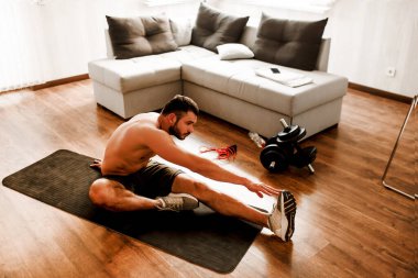 Genç adam spor için evine git. Spor figürlü tişörtsüz bir adam. Çekici elleriyle tek bacağına kadar geriniyor. Boş bir dairede tek başına alıştırma yapıyorsun. Formda kalmaya ve sağlıklı kalmaya çalış..