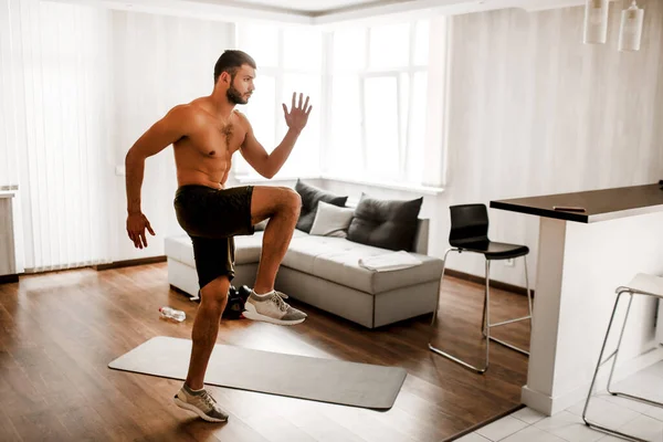 Genç adam evde, kanepede egzersiz yapıyor. Dairesinde spor yapan Hardwoing tişörtsüz adam. İyileşmeye çalışıyorum.