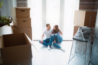 Evdeki oturma odasında genç evli bir çift pencerenin yanında oturuyorlar. Yeni evlerinden memnunlar. Taşınmak, ev almak, apartman konsepti..