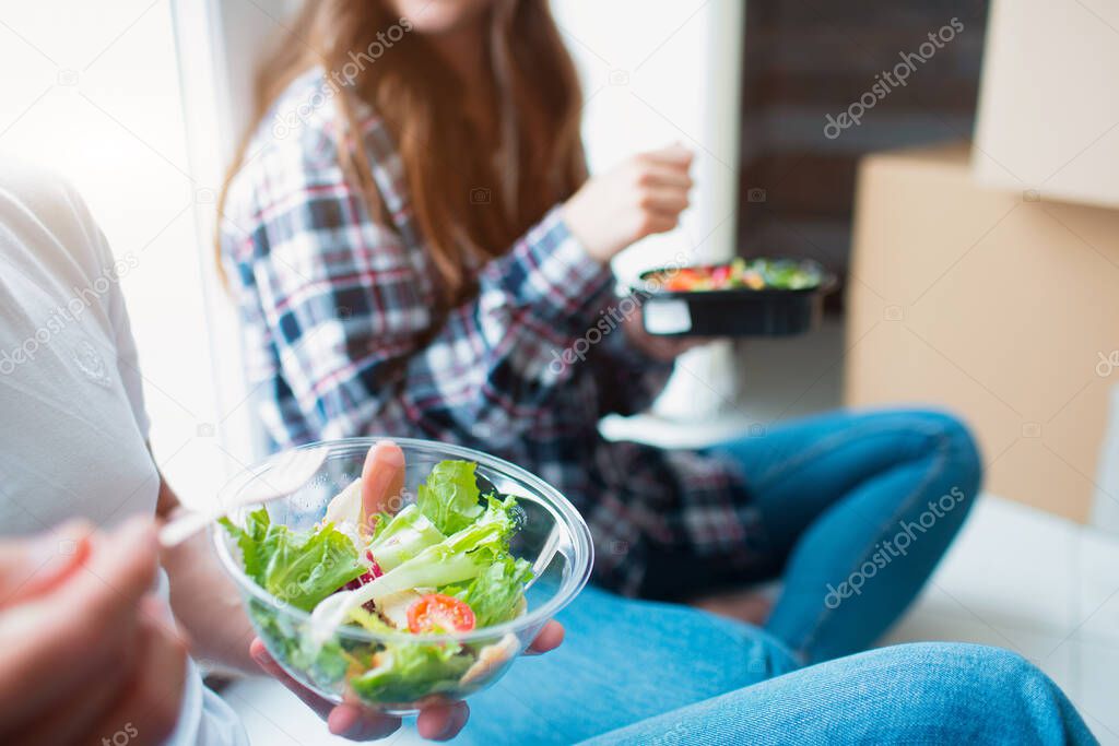 A young married couple in the living room in the house are sitting near the window and eat the first time in a new house. hey are happy about new home. Moving, buying a house, apartment concept.