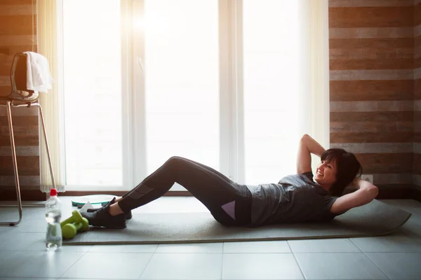 Vuxen passform smal kvinna har träning hemma. Väl formad senior kvinna gör abs motion. Ta hand om kroppen hålla sig ung och frisk. — Stockfoto