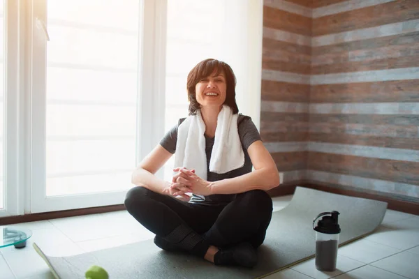 Vuxen passform smal kvinna har träning hemma. Sitt på yogamattan och håll äpplet i händerna. Snacktid efter träningen. Ta hand om hälsa och välbefinnande. — Stockfoto