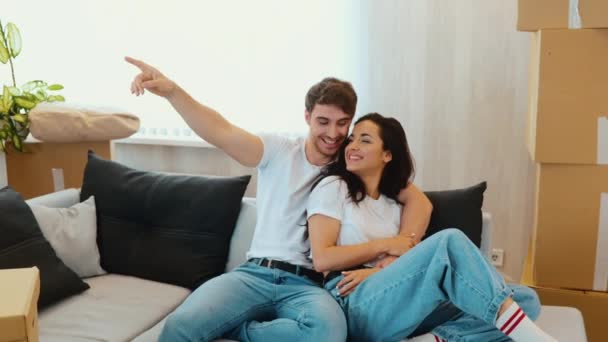 Junges Paar bezieht neue Wohnung Zeitlupe von Mann und Frau, die auf der Couch sitzen und gemeinsam Spaß haben. Kerl zeigt nach vorne und schaut seine Freundin an. — Stockvideo