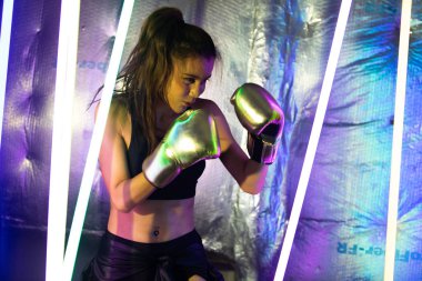 Güzel Asyalı Kadın Transseksüel Gümüş Altın Eldiven 'le antrenman yapıyor ve yumruk atıyor. Ofis kızı, modern renk Neon Muay Tayland Boks Salonu ile terli su sıçraması arasında güçlü duruyor.