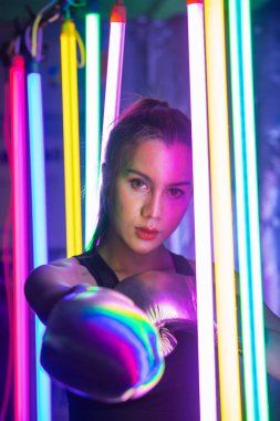 20 'li yaşlarda güzel bir Asyalı kadın yumruğu, gümüş altın eldivenlerle poz veriyor. Modern çok renkli Moda Neon Muay Tai Boks Salonu ve terli su sıçratma egzersizi