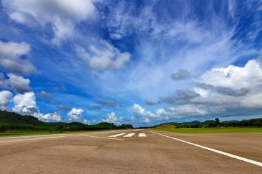 Beyaz çizgili havaalanı pist taksisi, yeşil dağ ve bulutlu mavi gökyüzü, kopyalama alanı
