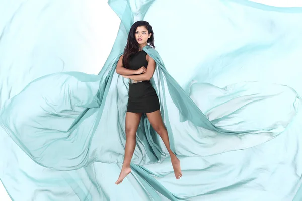 Tanned Skin Asian Woman wears Green Short Dress with chiffon fabric Fluttering throwing in Air, light see through, studio lighting white background isolated, jump float moving motion blur concept