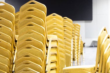 Yığınla Çelik Sandalye Kumaş Koltuk Sarı Altın Renk ve Masa büyük toplantı, konferans, atölye, gala yemeği, Otel Kongresi 'nde düğün töreni için sıraya dizilmeye hazır.