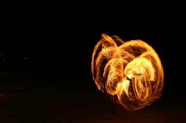 Yüksek Yetenekli Adam, odun direğini yakıt yağı ve ateşle döndürerek havai fişek gösterisi yapıyor. Tropikal adada okyanus boyunca ateş çemberi şeklinde daireler çiziyor.