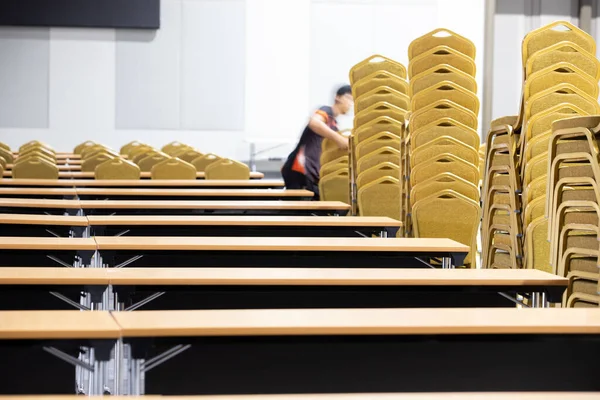 Stack Steel Chair Fabric seat pad yellow gold color and Table arrange in row ready to set up for big meeting, conference, business in Convention Hall of Hotel, worker carry chair with motion blur