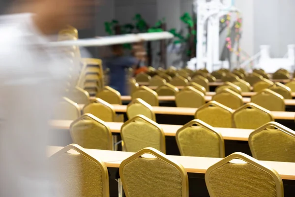 Stack Steel Chair Fabric seat pad yellow gold color and Table arrange in row ready to set up for big meeting, conference, business in Convention Hall of Hotel, worker carry chair with motion blur